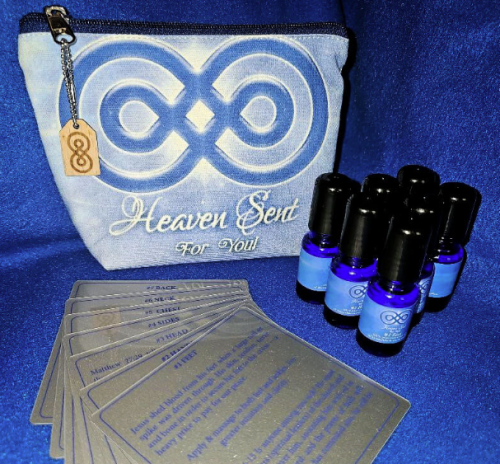 A Heaven Sent branded gift set displayed on a blue fabric background, featuring a zippered pouch with an infinity symbol and the words “Heaven Sent For You,” six small cobalt blue essential oil bottles, and several transparent cards with inspirational messages and scriptures.