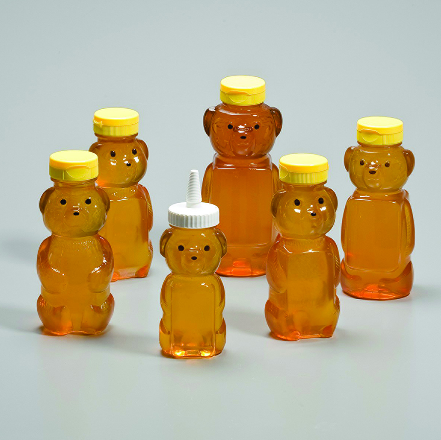 A group of clear plastic bottles in the shape of a bear with painted eyes and noses paired with two styles of dispensing caps in flip top and nozzle styles.